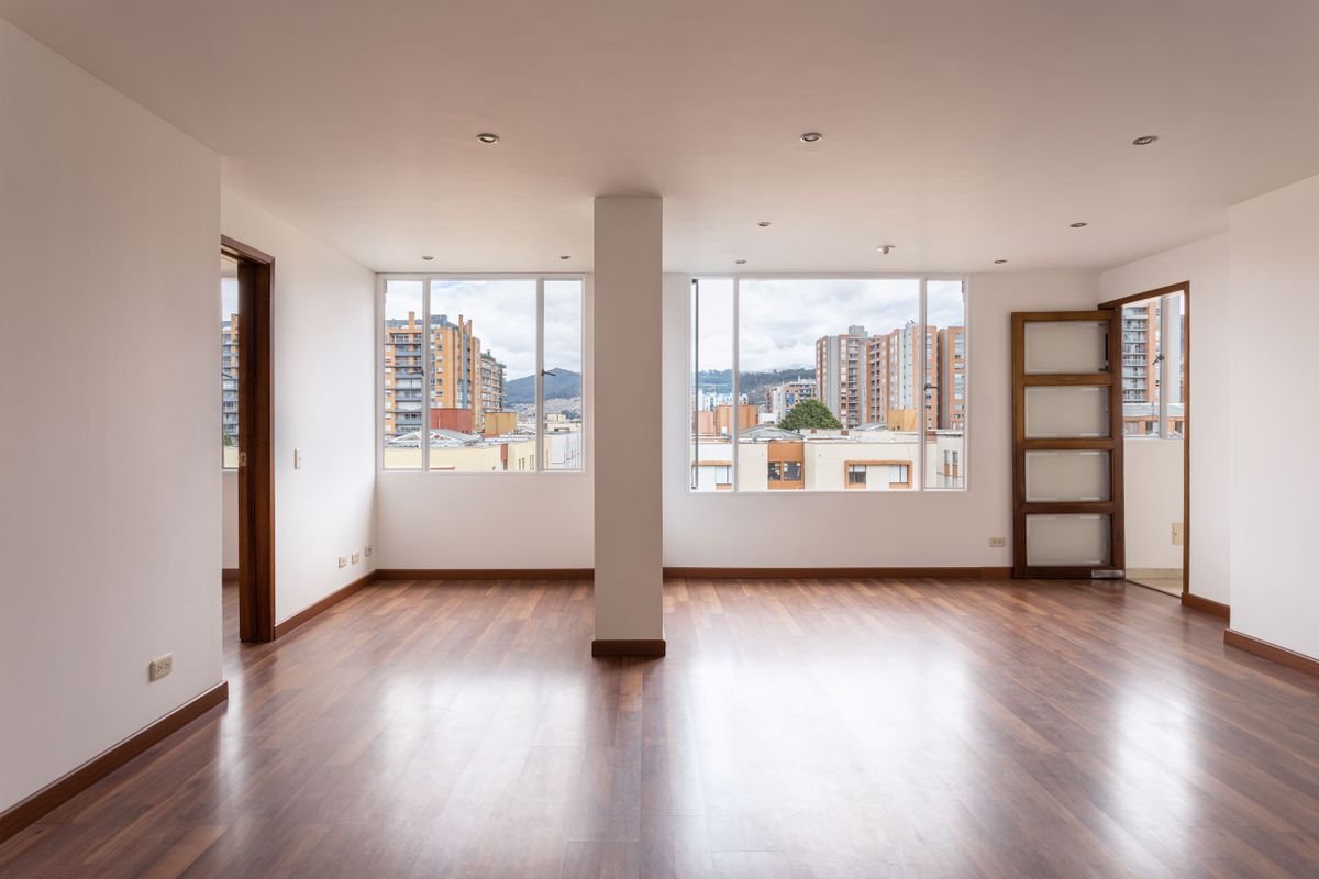 An empty condo living room with wooden flooring and large windows