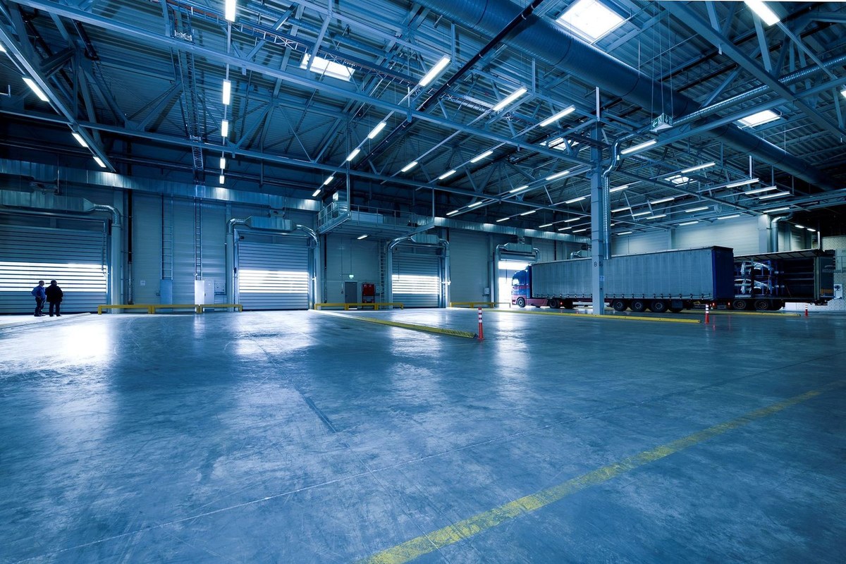 Large empty warehouse interior with blue overhead lights and rolling shutter loading docks